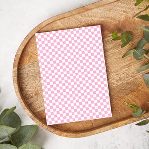 May include: A pink and white checkered card on a wooden tray with green leaves.
