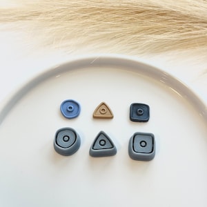 May include: Six small clay shapes in various colors, including blue, gray, and brown. The shapes are a circle, a triangle, and a square. Each shape has a smaller circle inside.