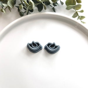 May include: Two grey plastic cookie cutters shaped like eyes. The cutters are on a white surface.