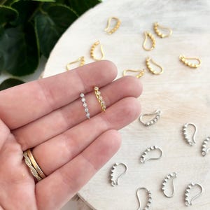 Puede incluir: Dos ganchos para pendientes con una fila de pequeños diamantes de imitación transparentes. Los ganchos son de metal y están disponibles en oro y plata.