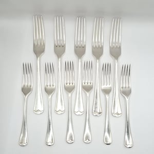 May include: A set of eleven silver-toned metal forks arranged in two rows. Each fork features four tines and a smooth, slightly flared handle with a rounded, heart-shaped base. The polished finish reflects light, creating a uniform appearance.