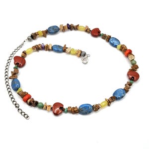 May include: A necklace featuring a variety of multi-coloured stone beads, including blue oval stones, red bear-shaped carvings, and small brown chip beads. The piece includes a silver-toned metal chain extender and a circular spring ring clasp.