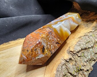 May include: A large, orange, white and brown agate crystal point, with a rough, natural finish, resting on a wooden slab.