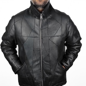 May include: A black leather jacket with a distinctive geometric patchwork pattern. The jacket has a high collar, a full-length zip, and two front pockets. The jacket is worn over a dark shirt and grey trousers.