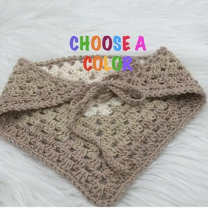May include: A crocheted triangle scarf in a beige and white color gradient. The text "CHOOSE A COLOR" is written in rainbow letters above the scarf.