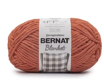 Puede incluir: Una gran madeja de hilo Bernat Blanket en color terracota cálido. La etiqueta dice "Bernat Blanket" e incluye detalles sobre el peso del hilo, 300 g. El hilo está hecho de 100% poliéster y está diseñado para hacer mantas.