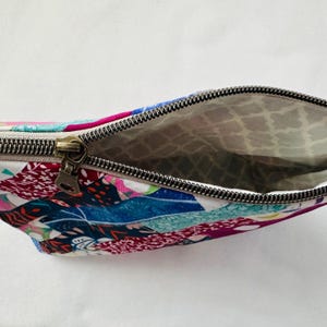 K&ouml;nnte beinhalten: Ein farbenfrohes T&auml;schchen mit Rei&szlig;verschluss und Patchwork-Design. Die Au&szlig;enseite zeigt eine lebendige Mischung aus floralen und abstrakten Mustern in Rosa-, Blau- und Gr&uuml;nt&ouml;nen. Das Innenfutter ist ein hellgraues Muster. Der Rei&szlig;verschluss ist aus dunklem Metall.