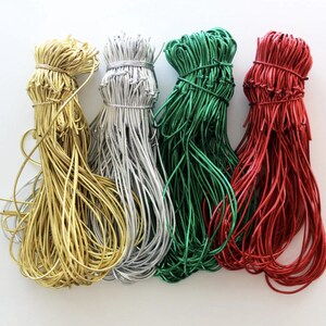 May include: Four bundles of metallic cord in gold, silver, green, and red. Each bundle is tied with a matching cord, with the strands fanning out. The cords are likely used for crafting, jewellery making, or gift wrapping.