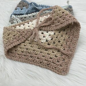 May include: A crocheted scarf in shades of beige, brown, and white. The scarf is made of a soft, textured yarn and has a fringed edge.