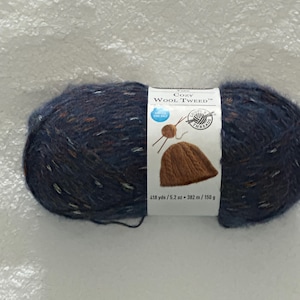 May include: A skein of blue yarn with flecks of white and brown. The yarn is labeled "Cozy Wool Tweed" and is 418 yards / 5.2 ounces / 382 meters / 150 grams.