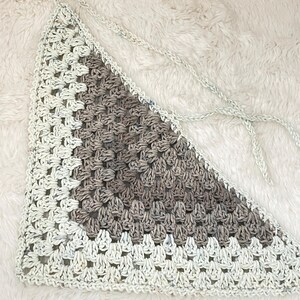 May include: A triangular crocheted piece with a white and brown color scheme. The piece is made with a square stitch pattern and has a fringe on the edges.