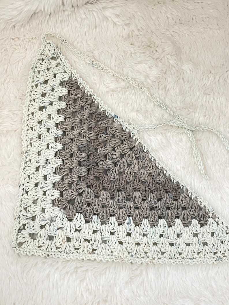 May include: A triangular crocheted piece with a white and brown color scheme. The piece is made with a square stitch pattern and has a fringe on the edges.