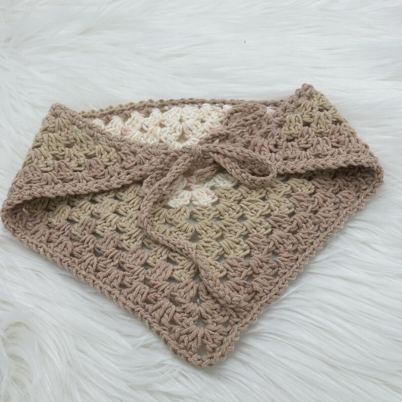 May include: A crocheted triangle scarf in beige and white with a knotted tie.