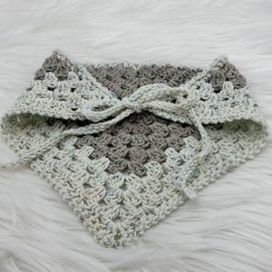 May include: A crocheted neck scarf with a white and gray color pattern. The scarf is tied with a bow in the front.