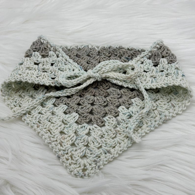 May include: A crocheted neck scarf with a white and gray color pattern. The scarf is tied with a bow in the front.