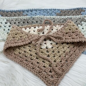 May include: A crocheted triangle scarf in beige, brown, and white with a tie closure. The scarf is made with a textured stitch pattern.