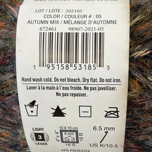 May include: A skein of yarn in a mix of autumn colors, including brown, orange, red, blue, and green. The yarn is labeled "Autumn Mix" and is made of 66% polyester, 30% acrylic, and 4% wool. The label also includes care instructions and information about the yarn's weight and size.