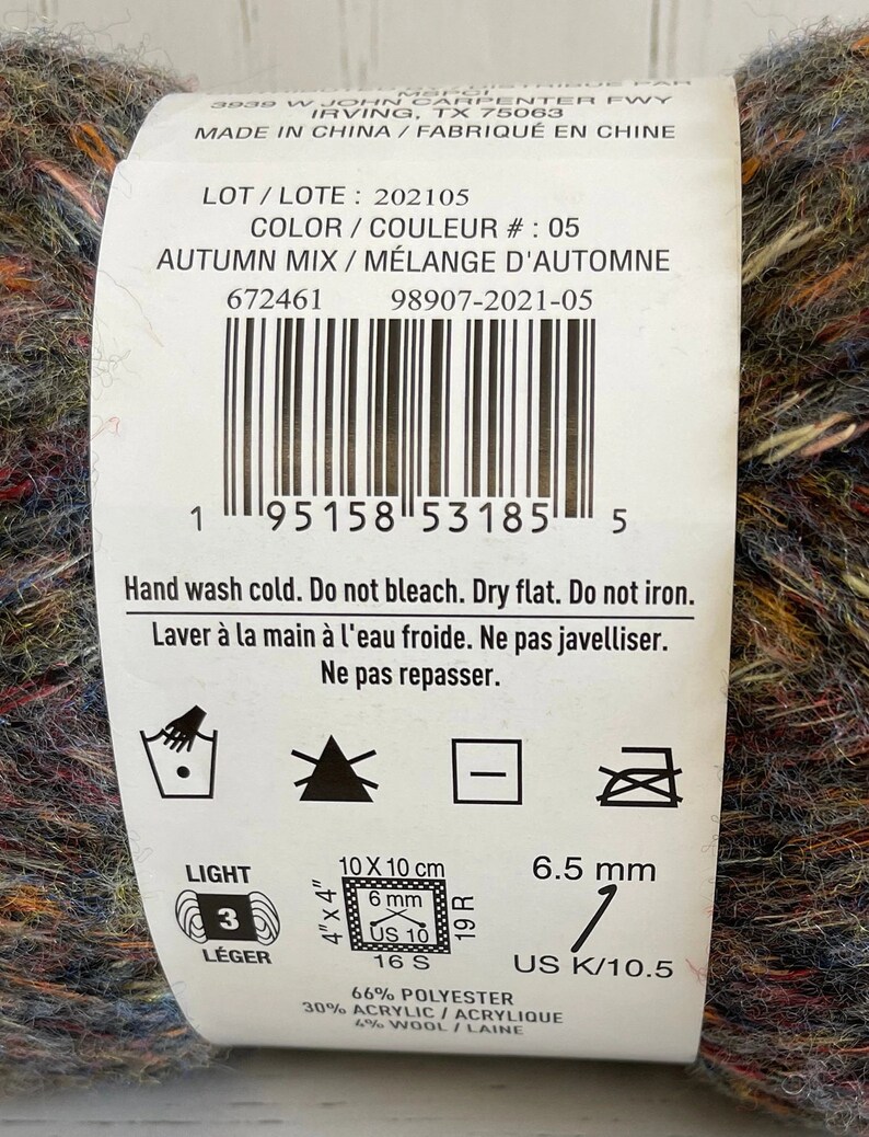 May include: A skein of yarn in a mix of autumn colors, including brown, orange, red, blue, and green. The yarn is labeled "Autumn Mix" and is made of 66% polyester, 30% acrylic, and 4% wool. The label also includes care instructions and information about the yarn's weight and size.