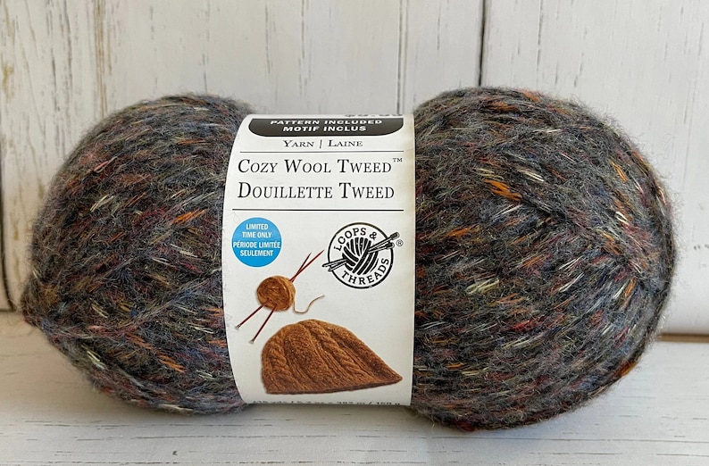 May include: A skein of Loops & Threads Cozy Wool Tweed yarn in the Douillette Tweed colorway. The yarn is a blend of wool and acrylic and has a tweed-like texture. The skein is labeled with the yarn name and colorway, as well as the brand name. The label also includes a pattern for a hat.