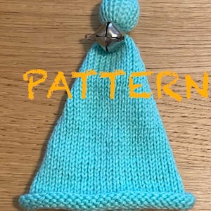 Puede incluir: Un gorro de punto azul claro con un pompón blanco y una campanilla plateada unida. El gorro tiene una textura acanalada y un borde doblado.