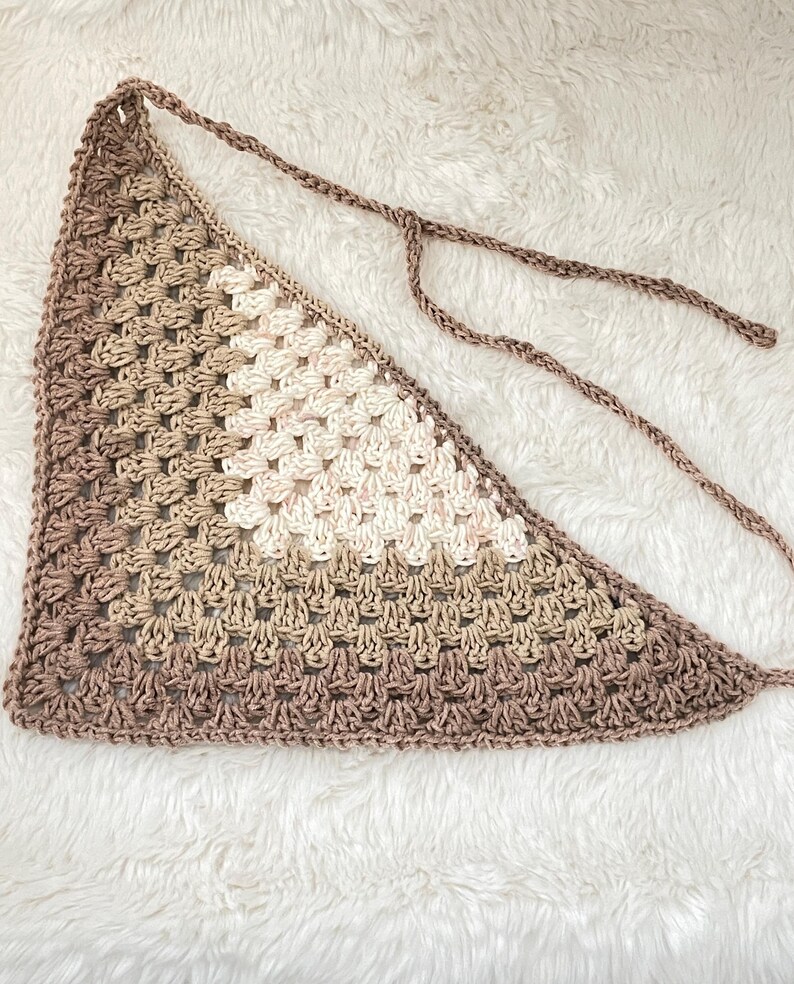 May include: A crocheted triangular scarf in shades of brown and white. The scarf has a fringe on the bottom edge and is tied with a long cord.