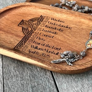 Peut inclure: Un plateau en bois avec un motif de croix celtique grav&eacute; dessus. Le plateau porte les mots "Wisdom, Understanding, Knowledge, Fortitude, Counsel, Piety, Fear of the Lord, William Marshall, April 6, 2025" grav&eacute;s dessus. Un chapelet argent&eacute; avec des perles grises repose sur le plateau.