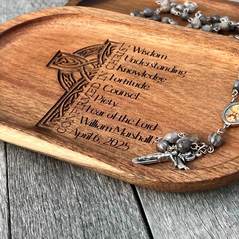 Peut inclure: Un plateau en bois avec un motif de croix celtique grav&eacute; dessus. Le plateau porte les mots "Wisdom, Understanding, Knowledge, Fortitude, Counsel, Piety, Fear of the Lord, William Marshall, April 6, 2025" grav&eacute;s dessus. Un chapelet argent&eacute; avec des perles grises repose sur le plateau.