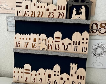 May include: Wooden Advent calendar featuring a cityscape design with numbers 1-24. The calendar has a dark blue background and a stone-like border. A small wooden nativity scene is also included.