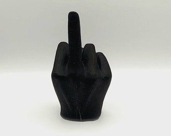 Può includere: Una scultura nera di una mano che fa il gesto del dito medio. La scultura è di colore nero pieno e sembra essere fatta di un materiale liscio. La mano è a pugno con il dito medio esteso verso l'alto.