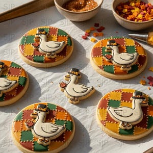 May include: Decorated sugar cookies with a Thanksgiving theme. Each cookie features a white duck wearing a black hat and holding a leaf, set against a colorful patchwork background. Sprinkles and small bowls are also visible.