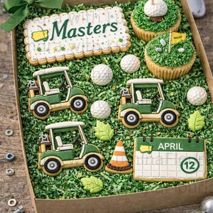 May include: A gift box containing golf-themed sugar cookies and cupcakes. The set includes three golf cart cookies, a rectangular cookie with the text Masters, a calendar cookie labelled April 12, a traffic cone cookie, and golf ball cookies.