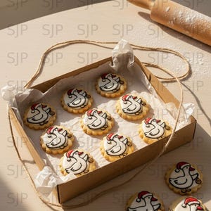 May include: A box of Christmas cookies with a duck design wearing a Santa hat. The cookies are round with a white icing base and a scalloped edge. A rolling pin and twine are also visible.