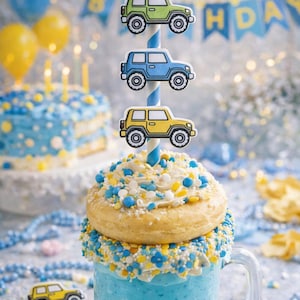 May include: A blue milkshake topped with a donut and colorful sprinkles, decorated with car-shaped toppers on a striped straw. A birthday cake and balloons are in the background. The theme is a birthday celebration.