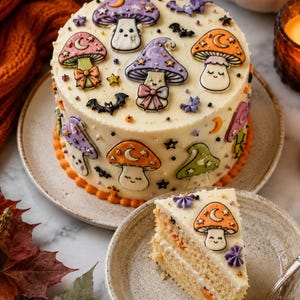 May include: A decorated cake with mushroom designs in orange, purple, and pink. The cake has a cream-colored frosting and is adorned with smiling mushroom figures, stars, and moons. A slice of the cake is on a plate, showing the layers.
