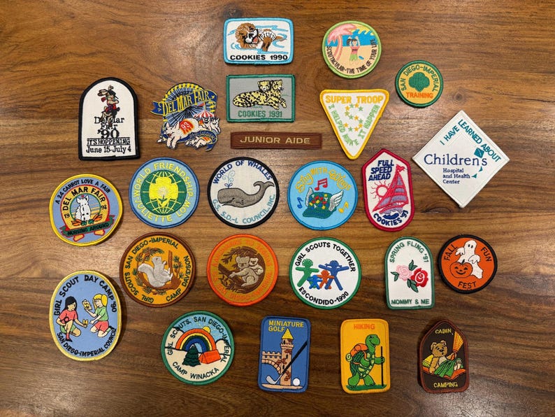 May include: A collection of vintage patches with various designs, including a tiger, a whale, and a cartoon turtle. The patches feature text such as "Cookies 1990", "Girl Scout Day Camp", and "Camp Winacka".