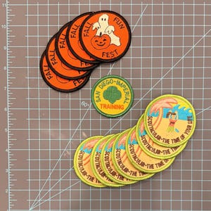 May include: A collection of embroidered patches. Several orange patches with "FALL FUN FEST" text and a ghost and pumpkin design. Other patches include "SAN DIEGO-IMPERIAL TRAINING" and "SCOUTACULAR - THE TIME OF YOUR LIFE" designs.