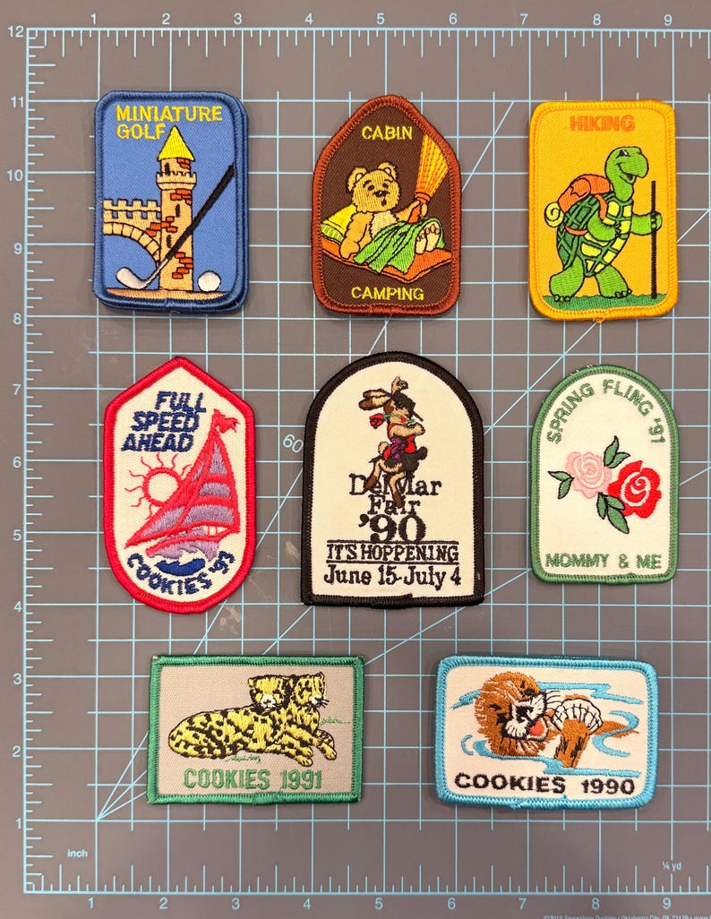 May include: A collection of embroidered patches with various designs. Themes include miniature golf, camping, hiking, sailing, and a fair. Some patches feature text like "COOKIES 1991" and "Del Mar Fair '90".