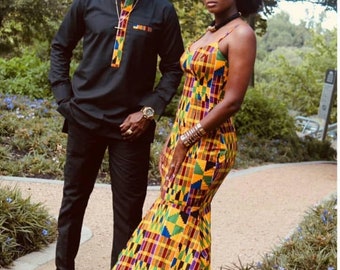 May include: A couple wearing matching black and yellow patterned outfits. The man is wearing a black long-sleeved shirt with a yellow and black patterned trim. The woman is wearing a yellow, black, red, and green patterned dress with a fitted bodice and a flowing skirt.