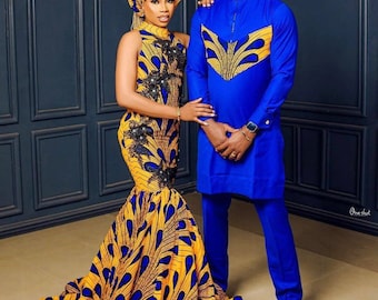 May include: A couple wearing matching blue and yellow patterned outfits. The woman is wearing a yellow and blue dress with a matching head wrap. The man is wearing a long-sleeved shirt and pants.