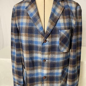 May include: A blue, brown, and white plaid blazer with a notched collar, three-button closure, and a chest pocket. The blazer is displayed on a mannequin. The fabric has a soft, textured appearance.