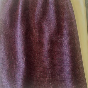 May include: A knee-length skirt in a deep plum purple hue, featuring a textured tweed fabric with subtle flecks of red, blue, and black throughout. The garment has a simple, straight-cut silhouette with an elasticized waistband at the top.