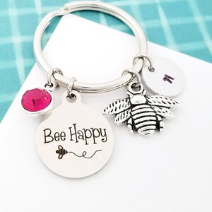 May include: A silver keychain with a bee charm, a pink crystal, and a round tag that says "Bee Happy".