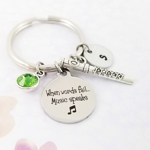 May include: Silver keychain with a green crystal charm, a silver flute charm, and a round charm with the text "When words fail... Music speaks" and a musical note symbol.