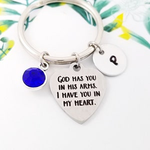May include: A silver heart-shaped keychain with the text "God has you in his arms. I have you in my heart."  A blue crystal charm and a silver charm with the letter "P" are attached to the keychain.