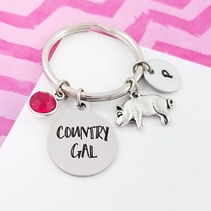 May include: Silver keychain with a pig charm, a red rhinestone, and a round charm with the text "COUNTRY GAL".