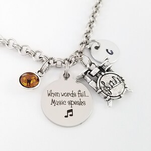 May include: Silver necklace with a charm that says "When words fail... Music speaks" and a musical note. The necklace also has a small drum charm and a brown crystal charm.