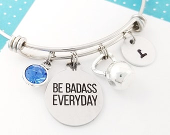 May include: Silver expandable bangle bracelet with a blue crystal charm, a silver charm with the text "BE BADASS EVERYDAY", a silver kettlebell charm, and a silver charm with the letter "I".