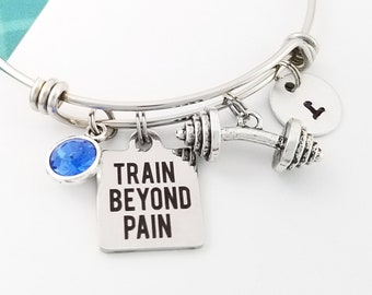 May include: Silver charm bracelet with a blue crystal, a dumbbell charm, and a charm with the text "TRAIN BEYOND PAIN".