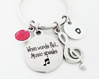 May include: Silver keychain with a charm that says "When words fail... Music speaks" with a musical note, a silver treble clef charm, a red rhinestone charm, and a silver charm with the letter "D".
