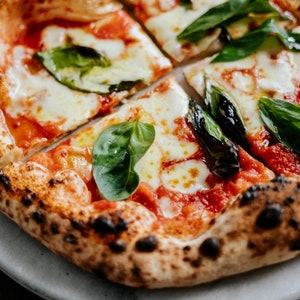 May include: A close-up of a pizza with a crispy crust, red sauce, melted mozzarella cheese, and fresh basil leaves.